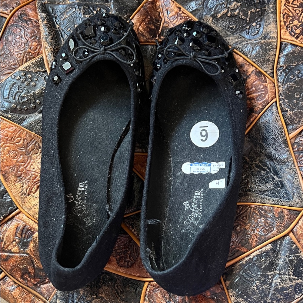Black flat ballerinas with black shiny embellishments.
6